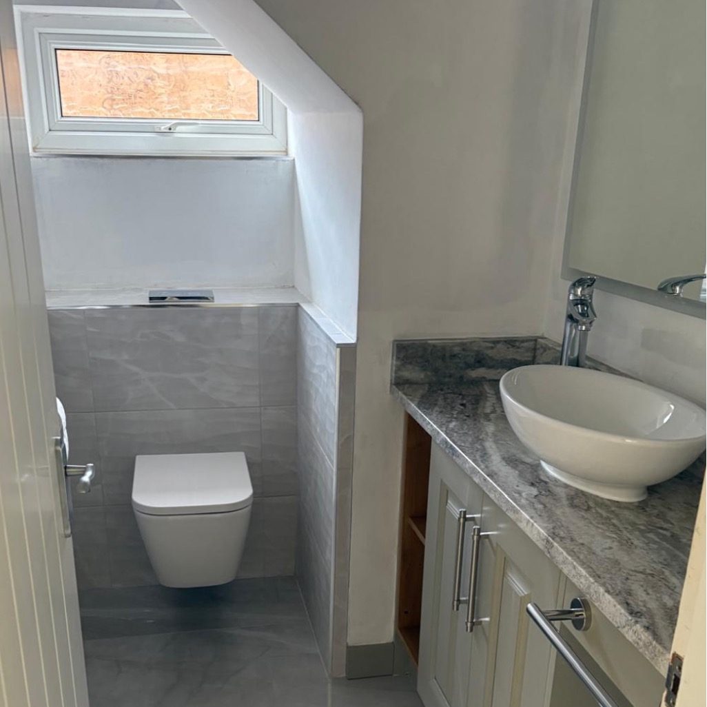 Finished cloakroom with a wall-hung WC, concealed cistern, grey marble-effect tiling and a vanity with countertop basin by AGG Renovations