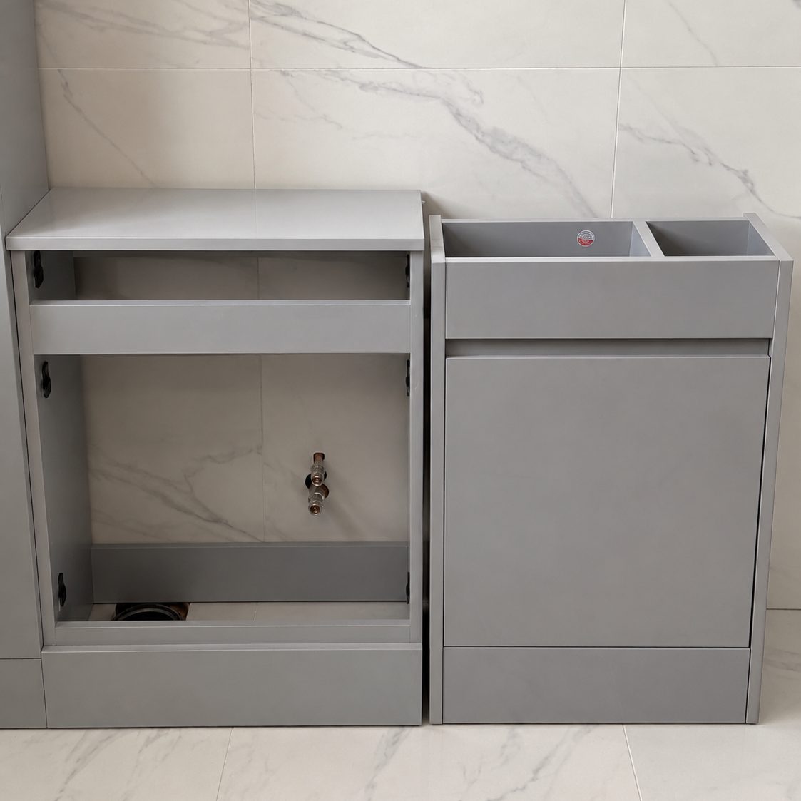 Bathroom vanity units being installed against the new marble-effect tiling, carcasses open with no doors, worktop or basin
