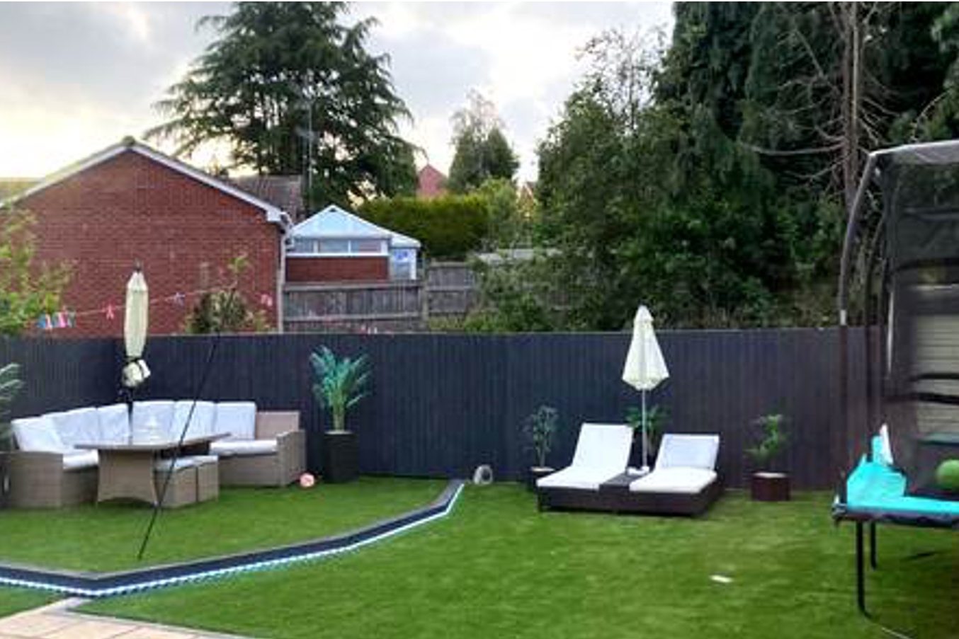 Finished rear garden with artificial lawn, dark grey fencing, a seating area and sun loungers by AGG Renovations