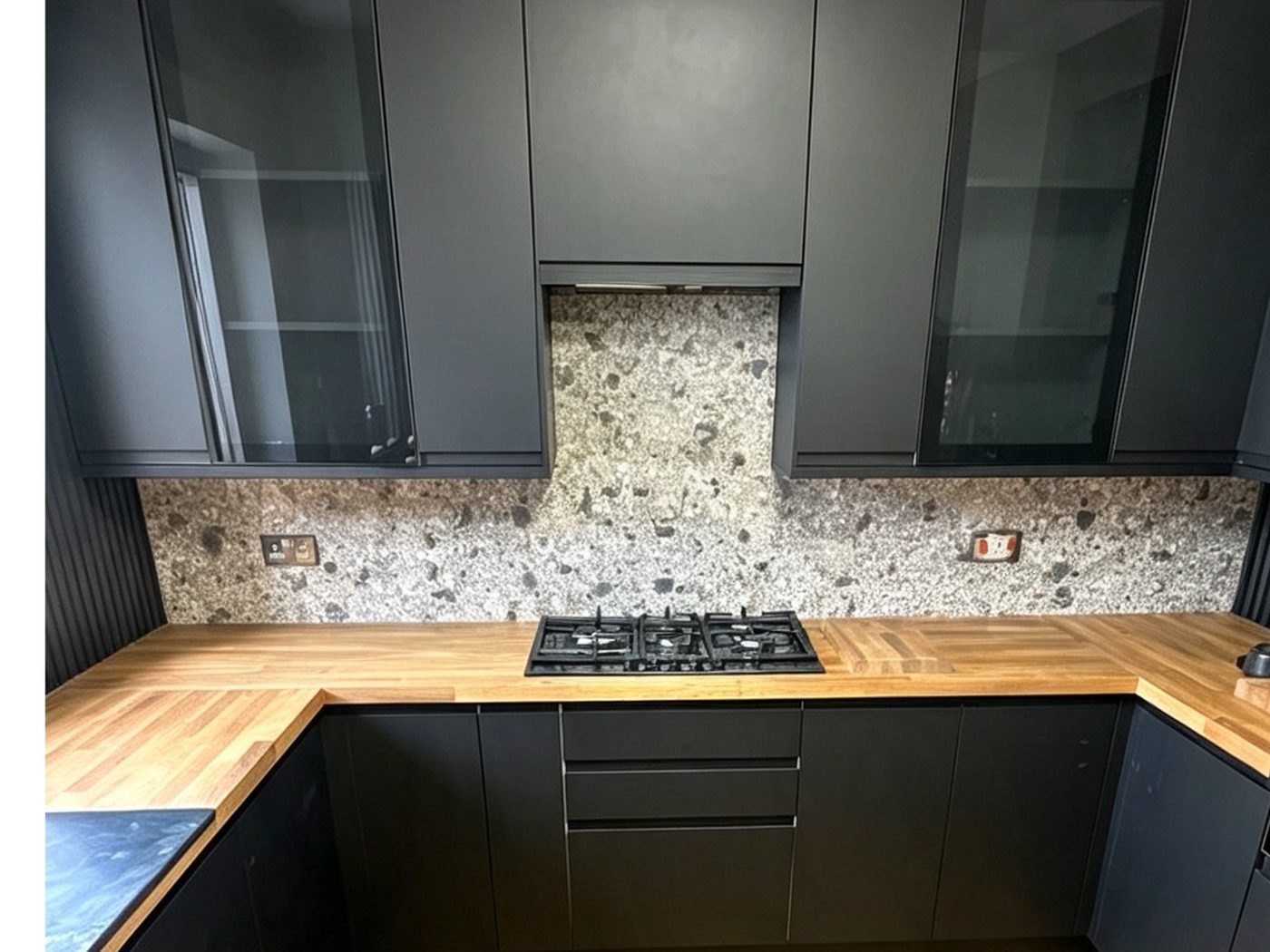 Finished matt black kitchen with a speckled granite splashback, fitted extractor and solid oak worktops by AGG Renovations