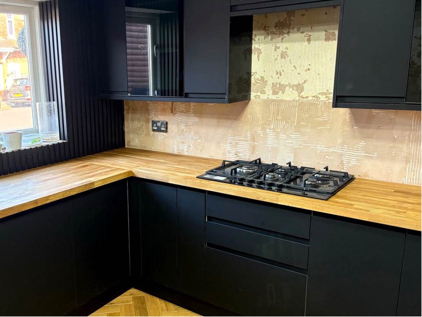 Matt black kitchen part-finished, with bare tile adhesive behind the hob and no extractor fitted
