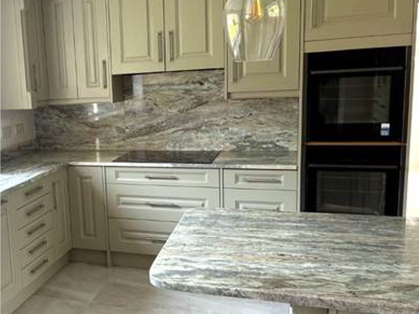 Finished sage shaker kitchen with veined marble worktops, matching splashback and a double oven by AGG Renovations