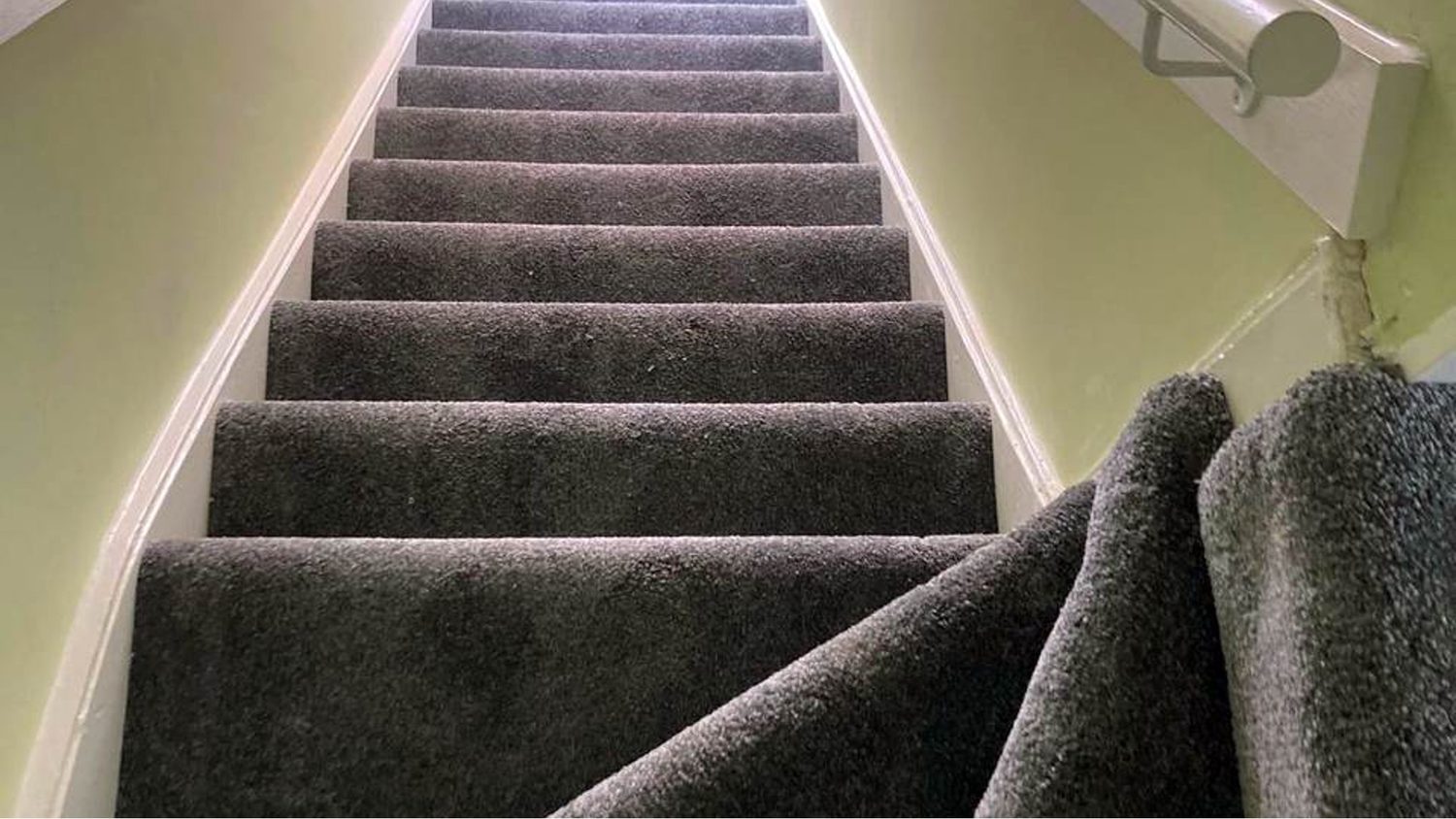 Grey carpet being fitted to a staircase, laid tight to every nosing