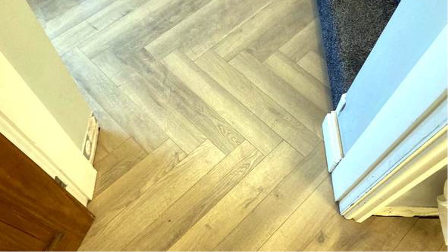 Herringbone wood-effect flooring running from a hallway through a doorway