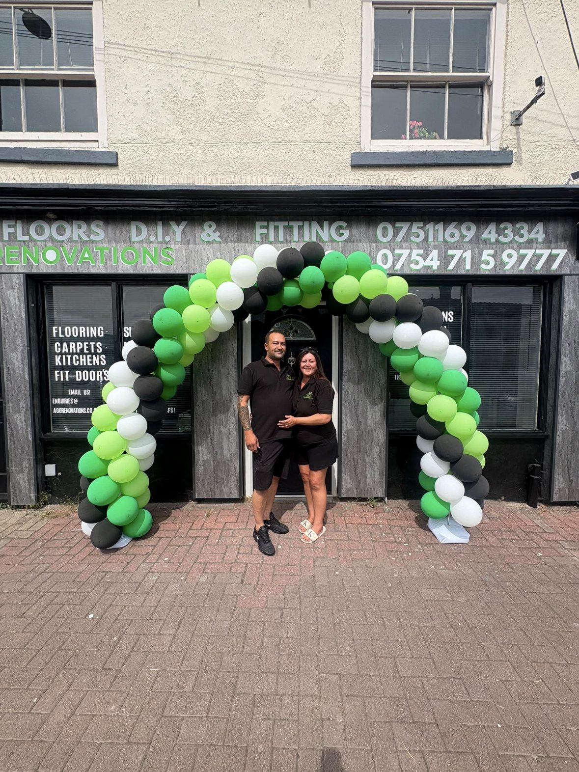 Mr and Mrs Green outside the AGG Renovations shop on opening day, under a green, black and white balloon arch